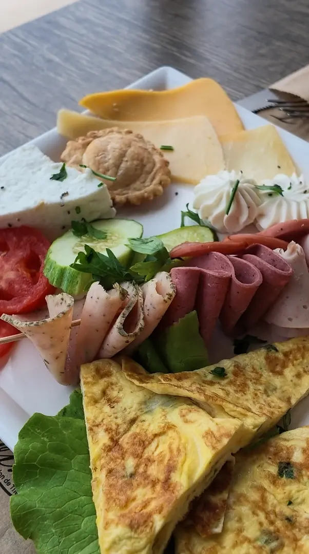 Une assiette de brunch : fromages, omelette, charcuterie roulée, tomate, concombre et chantilly salée.