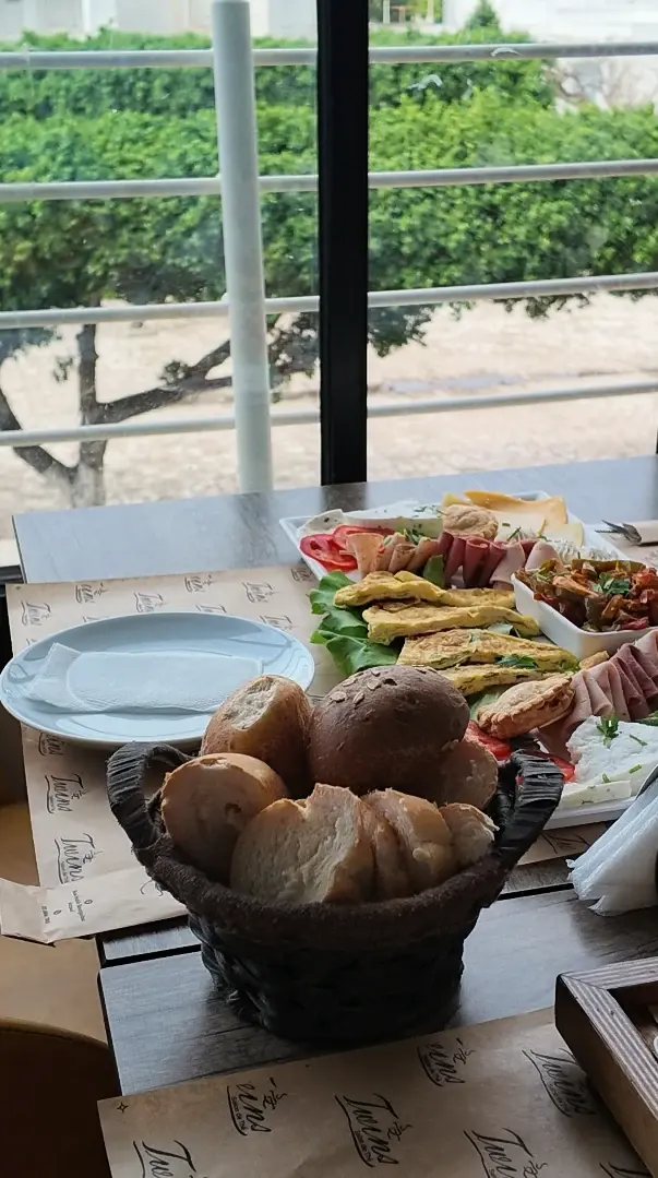 Un brunch dressé devant la baie vitrée : corbeille de pains, plateaux d'omelette, de charcuterie et de fromages.