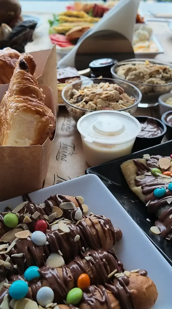 Crêpes roulées nappées de chocolat, d'amandes effilées et de bonbons colorés, devant les croissants et les bols du brunch.