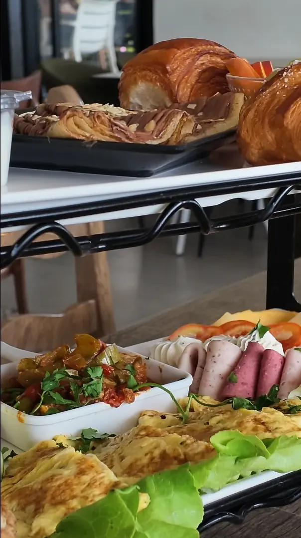 Présentoir de brunch : croissants et feuilletés au chocolat en haut, omelette, charcuterie roulée et salade en bas.