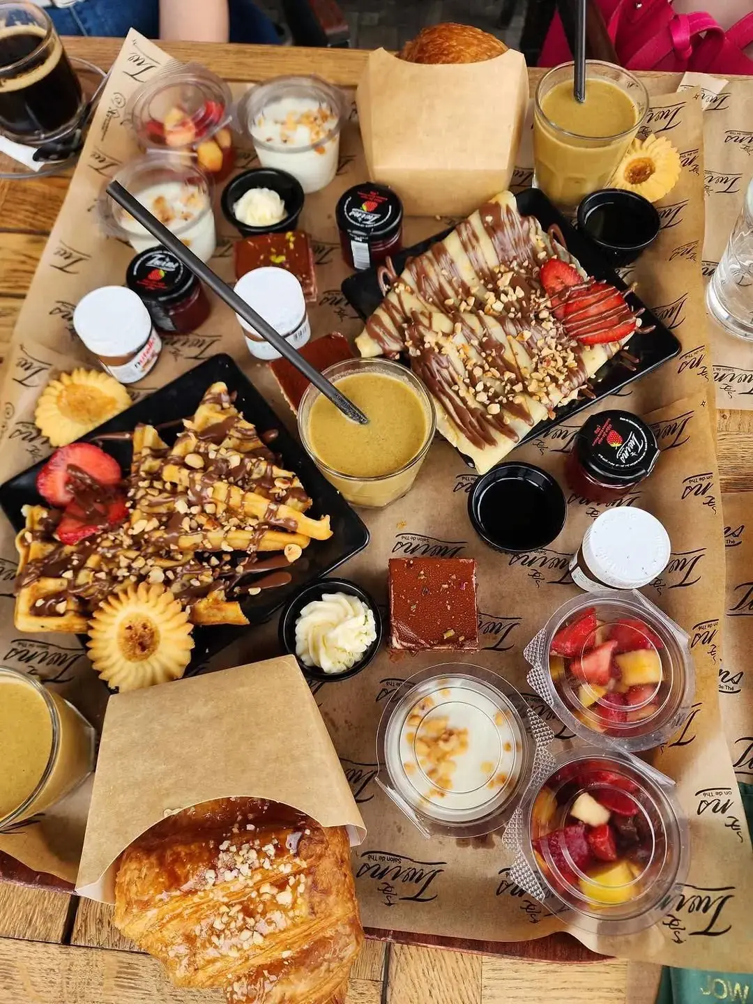 Brunch à partager sur papier kraft Twins : gaufres, croissants, yaourts, salade de fruits et jus d'orange.