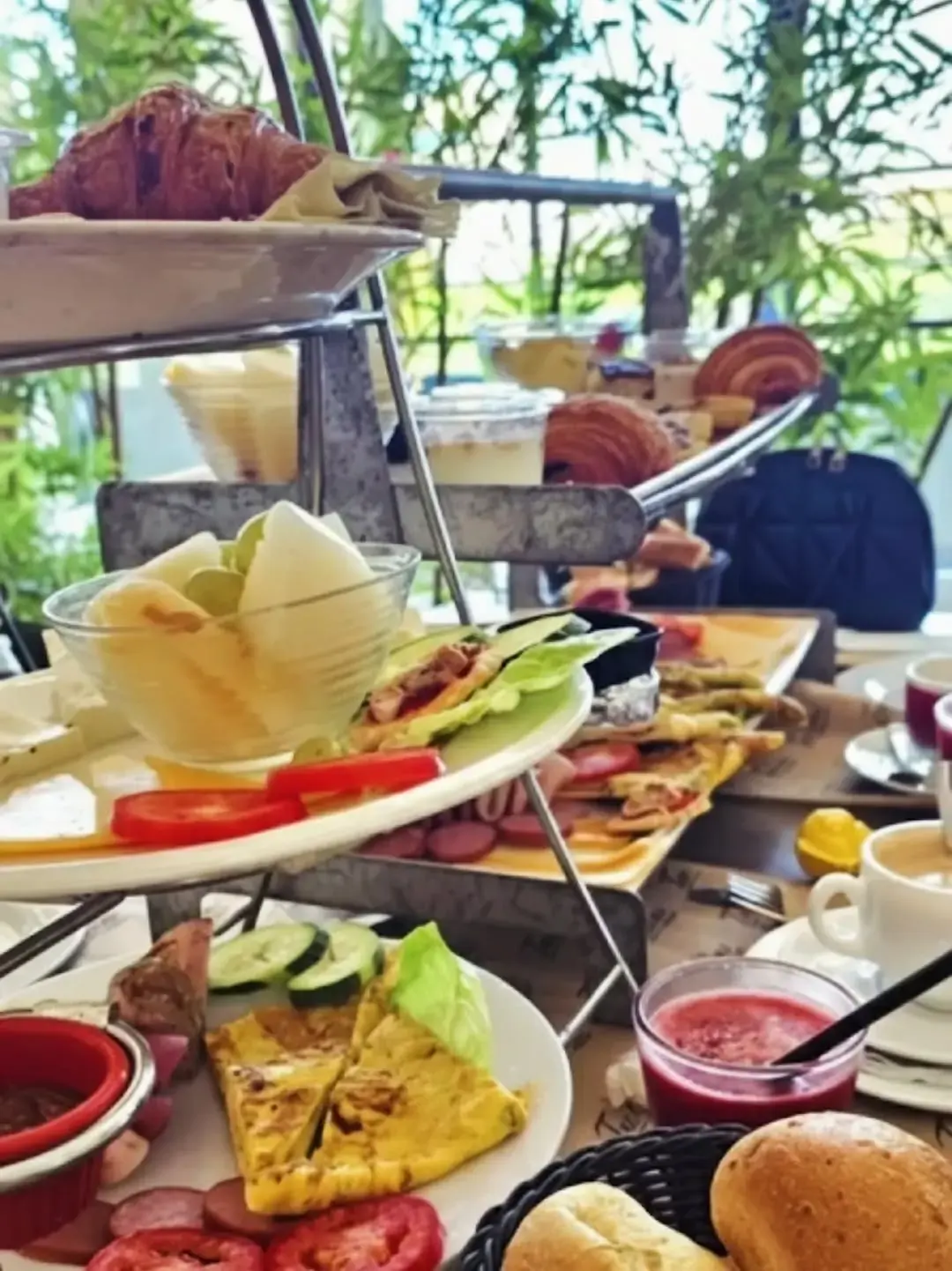 Plateau de brunch à étages : omelette, charcuterie, fromages, croissants et café, dressé en terrasse.