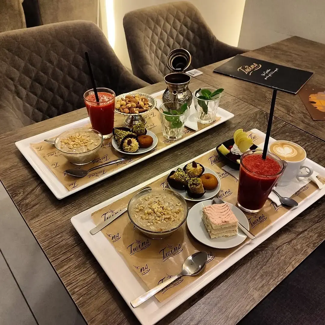 Deux plateaux de petit-déjeuner : jus de fraise, café, bsissa, mignardises et part de gâteau.