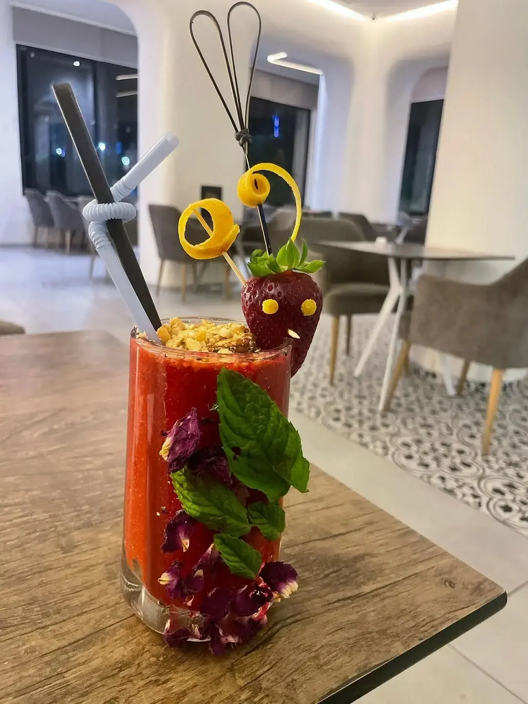 Cocktail de fraise décoré de menthe, de zestes d'orange et de pétales, sur une table en bois.
