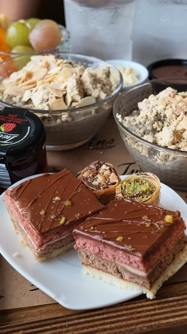 Deux parts d'entremets à étages rose et chocolat, glaçage brillant et éclats de pistache, avec deux pâtisseries feuilletées aux fruits secs.