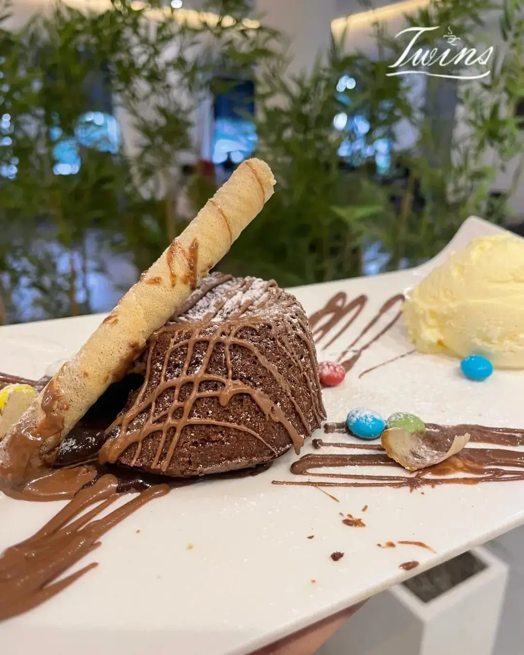 Fondant au chocolat nappé de sauce, accompagné d'une boule de glace vanille et d'une tuile roulée.