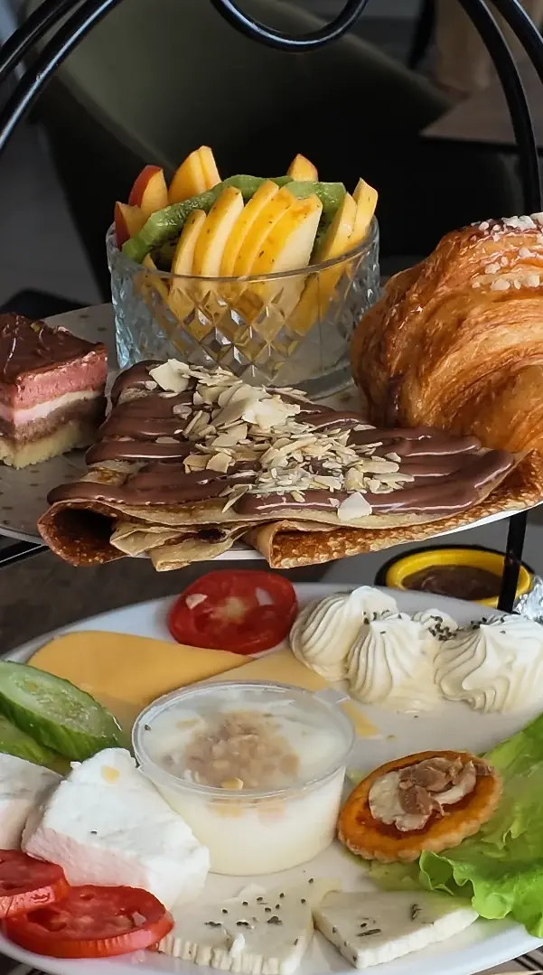 Gros plan d'un présentoir : crêpe au chocolat et amandes, croissant, fruits frais, fromages et chantilly.