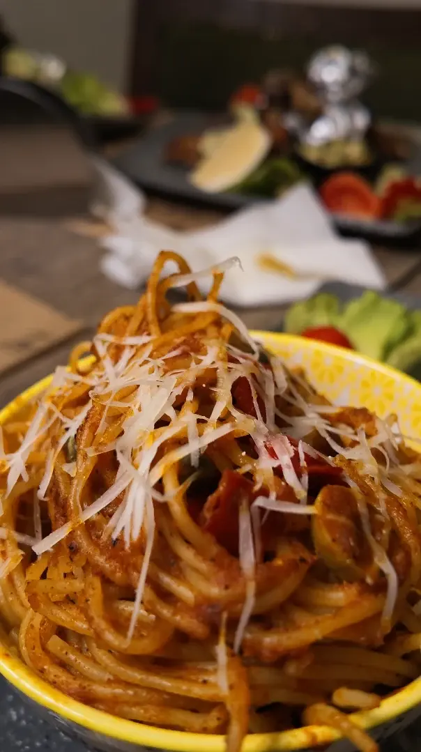 Des spaghetti à la sauce tomate et aux olives, couverts de fromage râpé, dans un bol jaune.