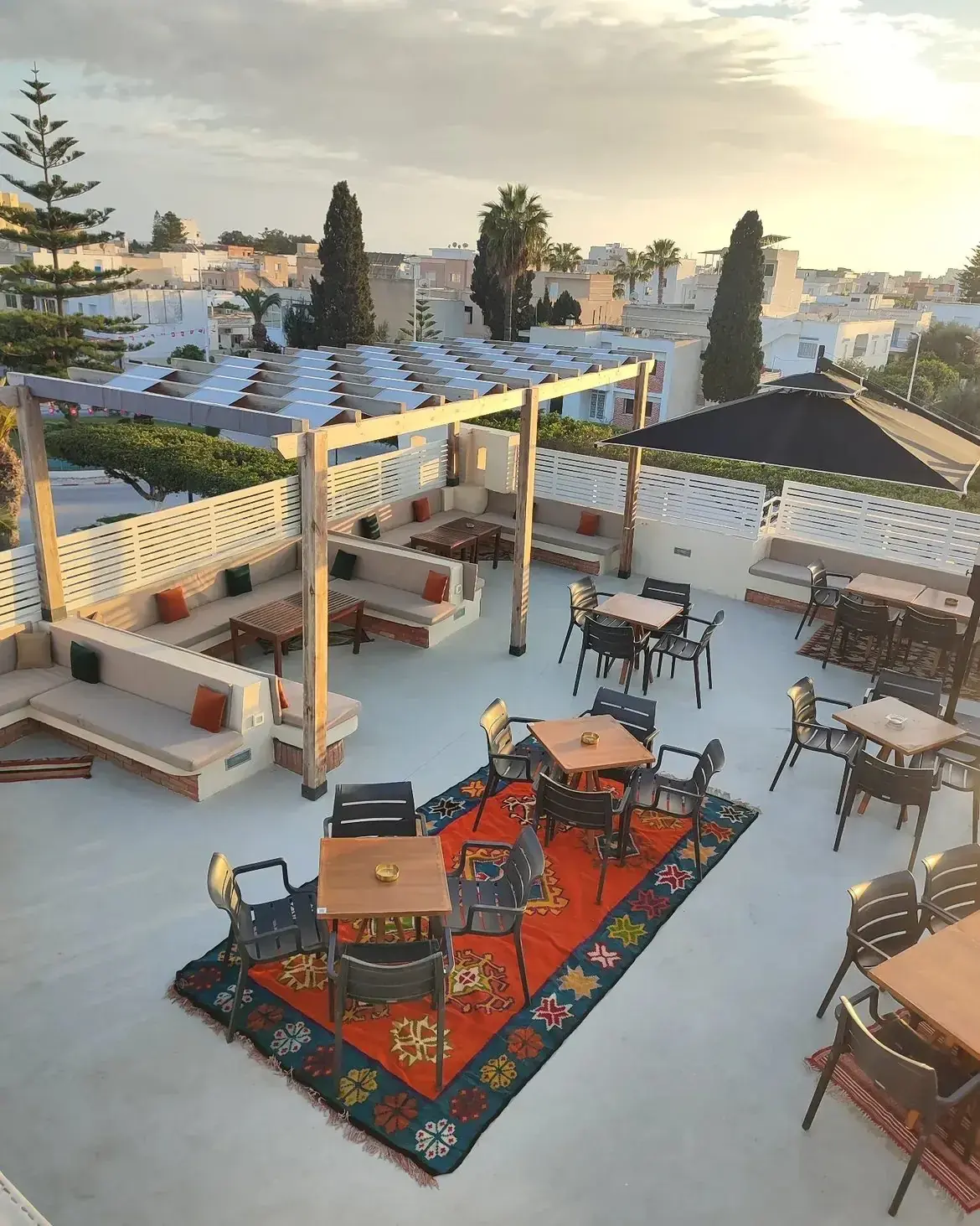 La terrasse sur le toit du Twins au coucher du soleil : banquettes basses, tapis colorés et pergola en bois.