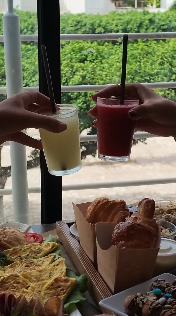 Deux verres levés, un jus de citron et un jus rouge, au-dessus d'une table de brunch face à la verdure.