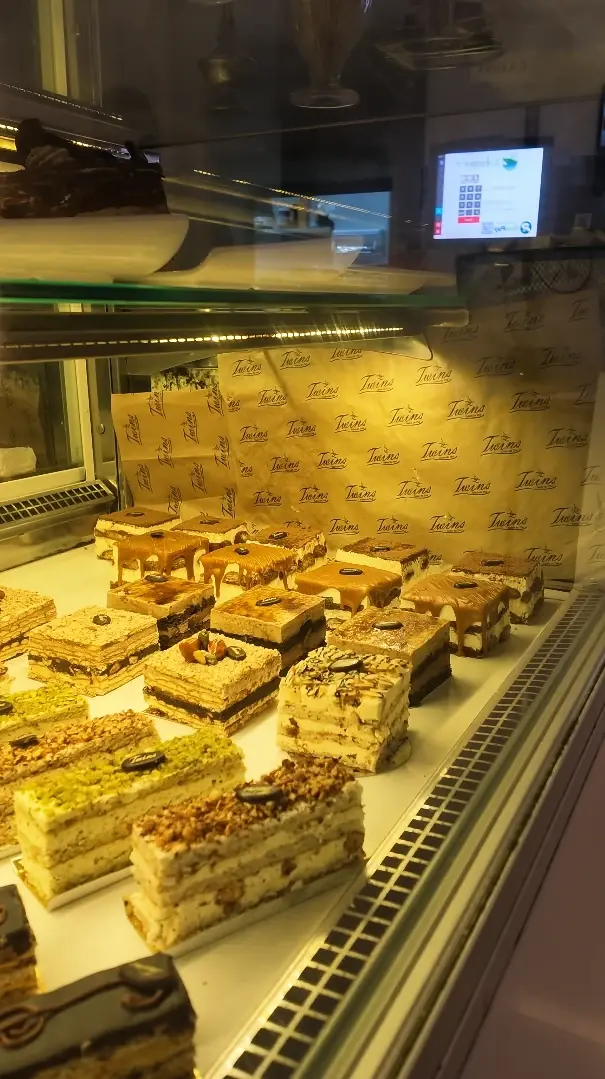 La vitrine du Twins : parts d'entremets au café, à la pistache et au chocolat, sur papier imprimé Twins.